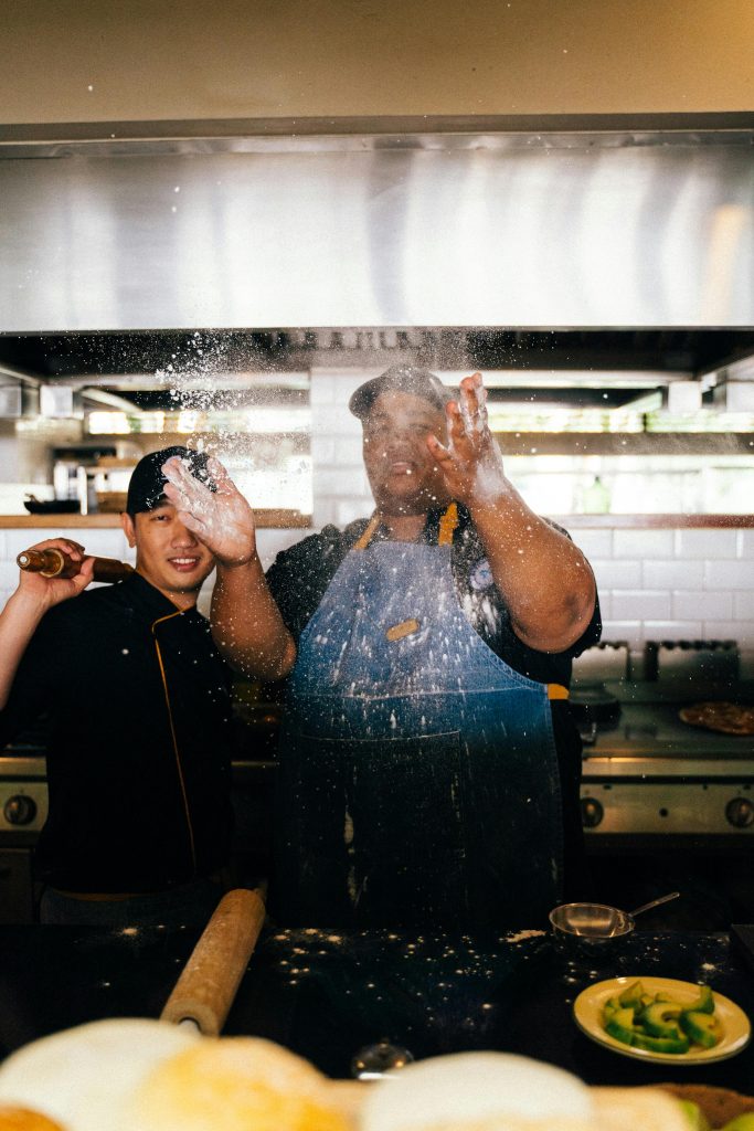 pexels-photo-6937417-6937417 Two chefs energetically preparing food in a vibrant kitchen setting.